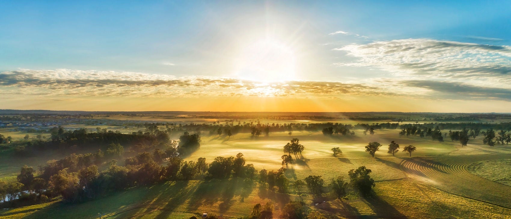 Secluded farm homestead on agriculture cultivated fields near Macquarie river in Dubbo town of Australia - aerial sunrise view.